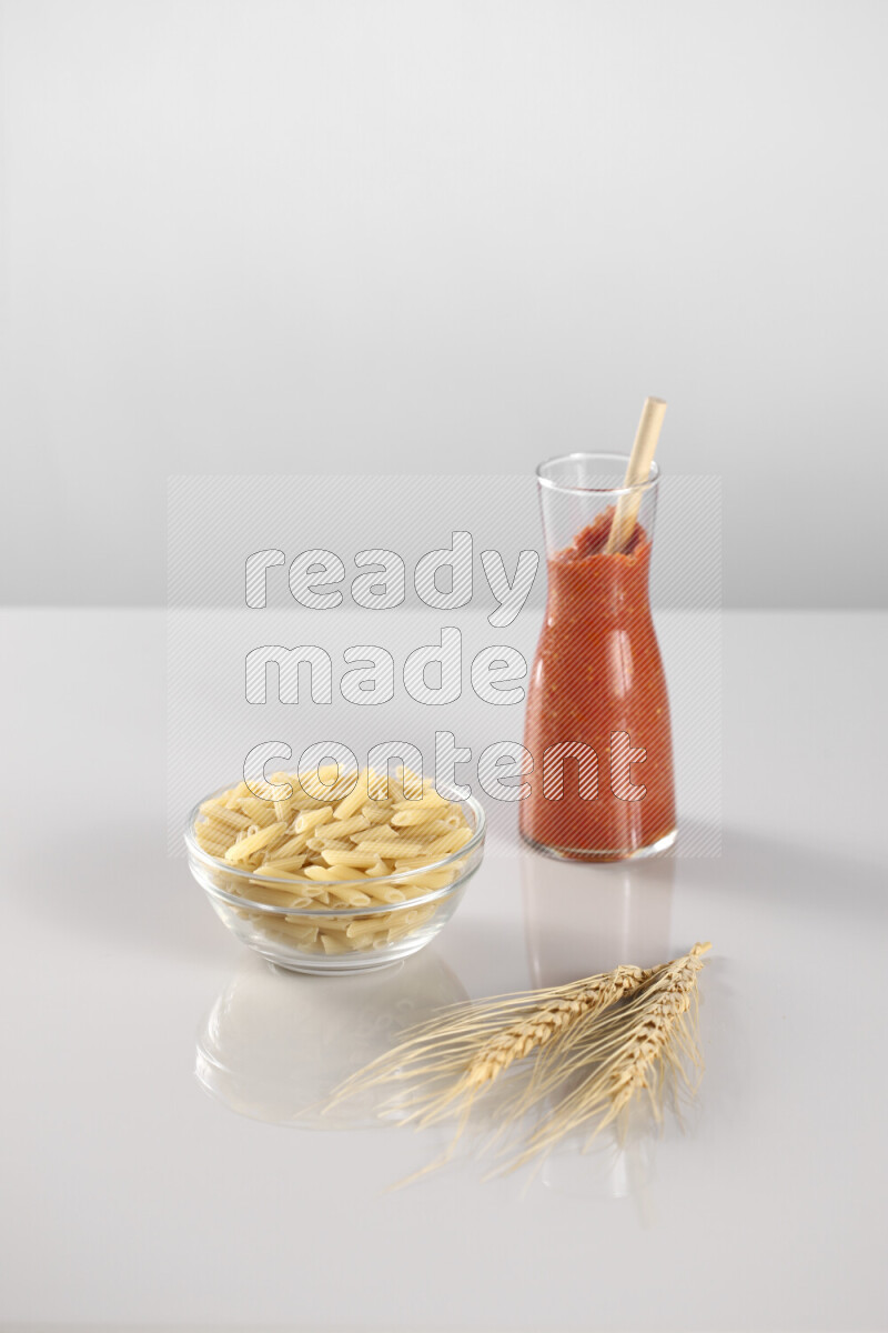 Raw pasta with tomatoe pasta with different ingredients such as cherry tomatoes, basil, garlic, bay laurel, cardamom, white pepper, black pepper, red chilis and wheat stalks on light grey background