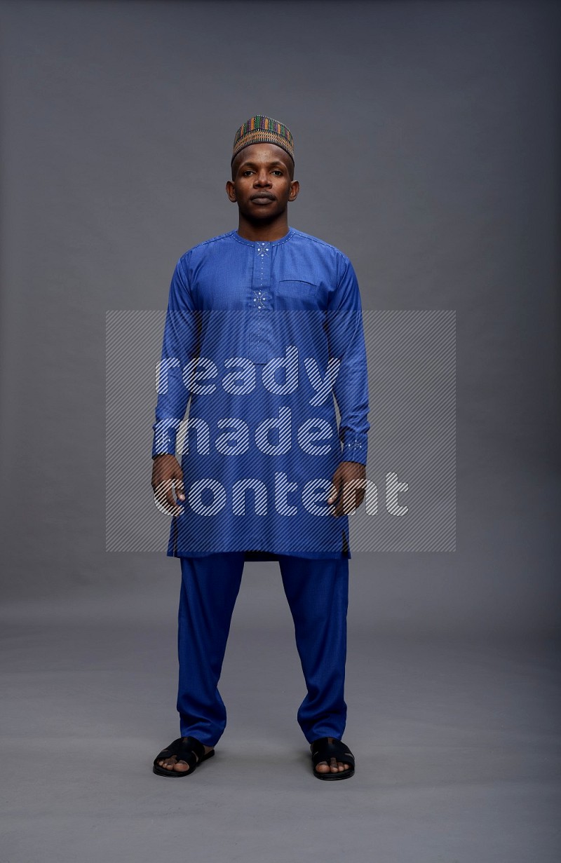 Man wearing Nigerian outfit standing interacting with the camera on gray background