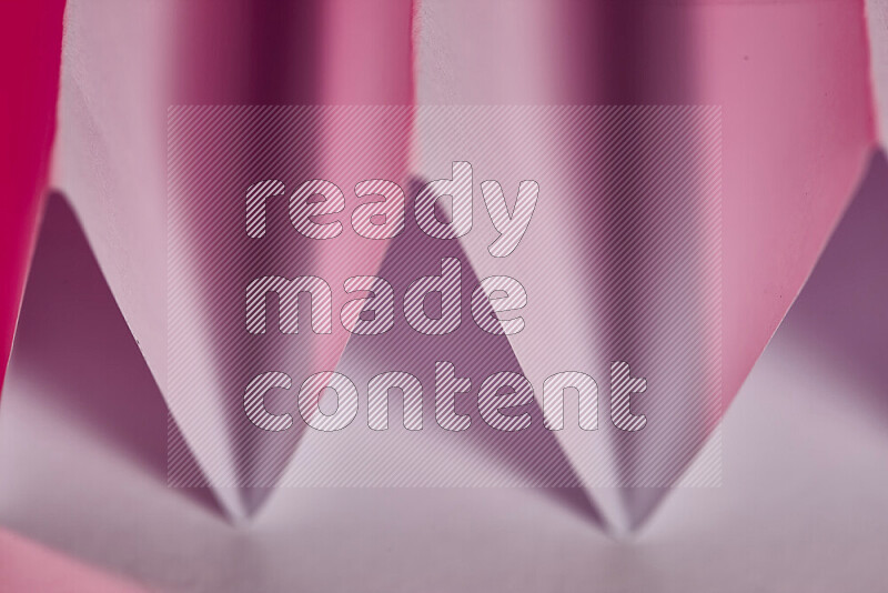 A close-up abstract image showing sharp geometric paper folds in pink gradients