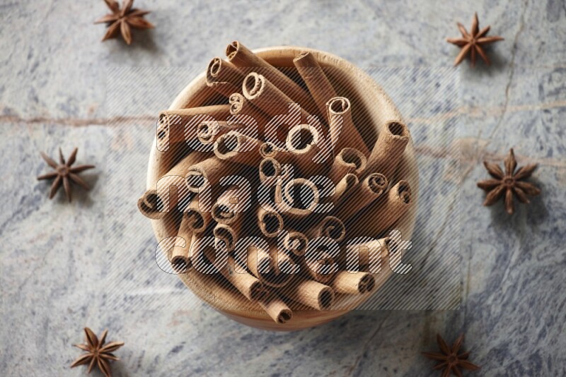 wooden bowl full of cinnamon sticks surrounded by star anis on marble background in different angles