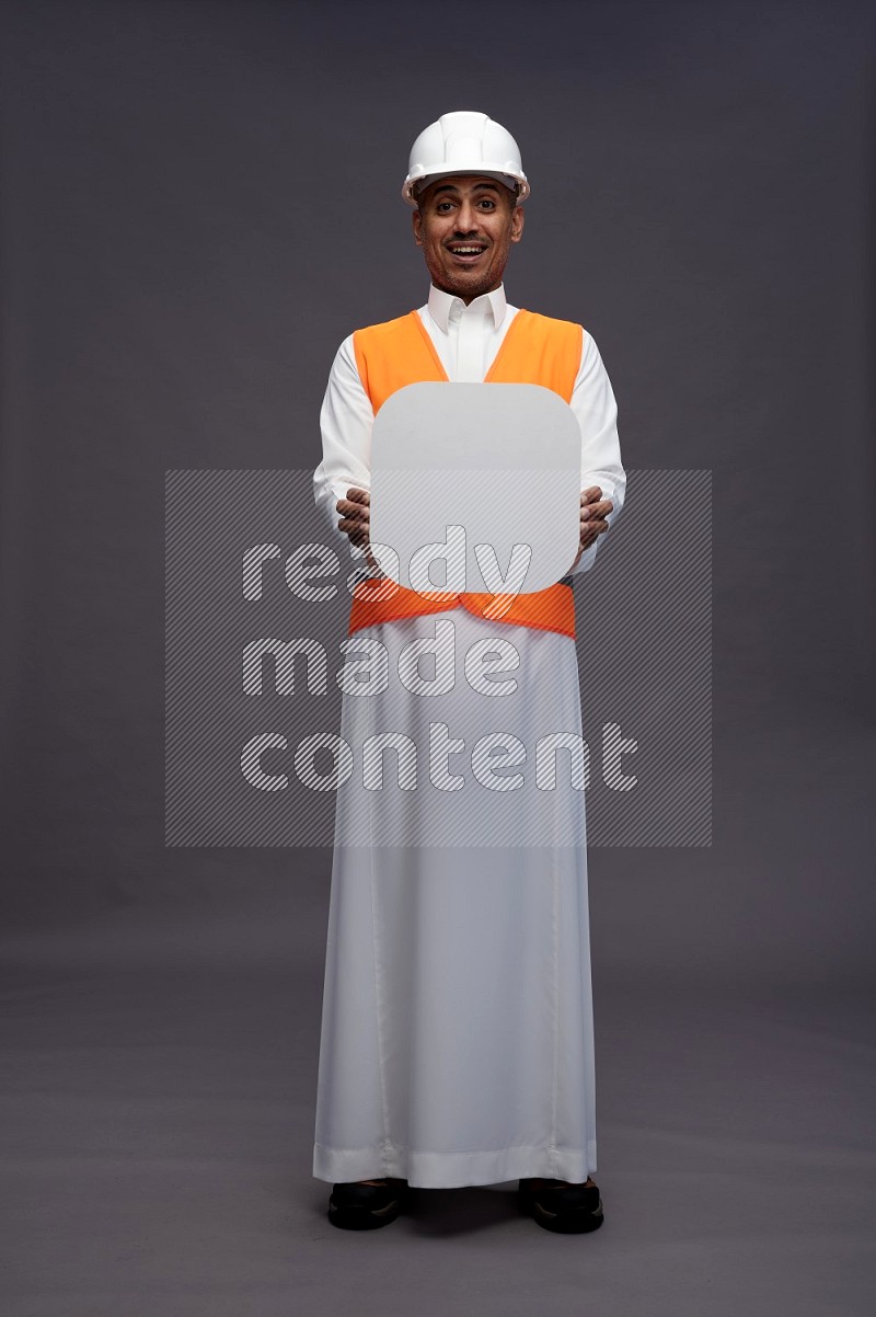 Saudi man wearing thob with engineer vest standing holding social media sign on gray background