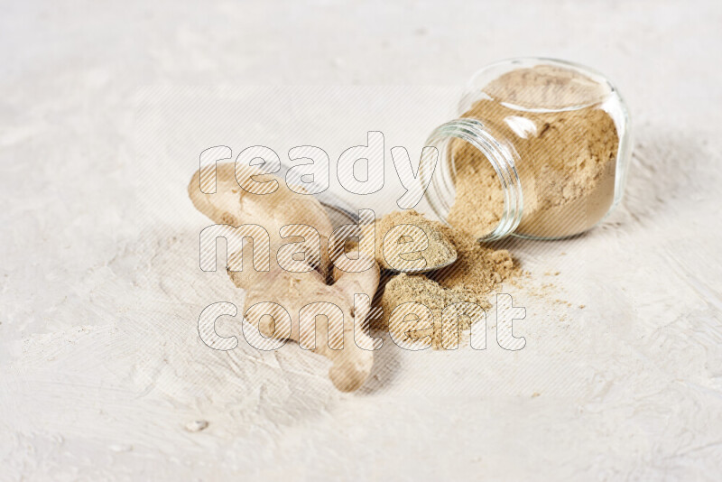 A glass jar full of ground ginger powder flipped with some spilling powder on white background