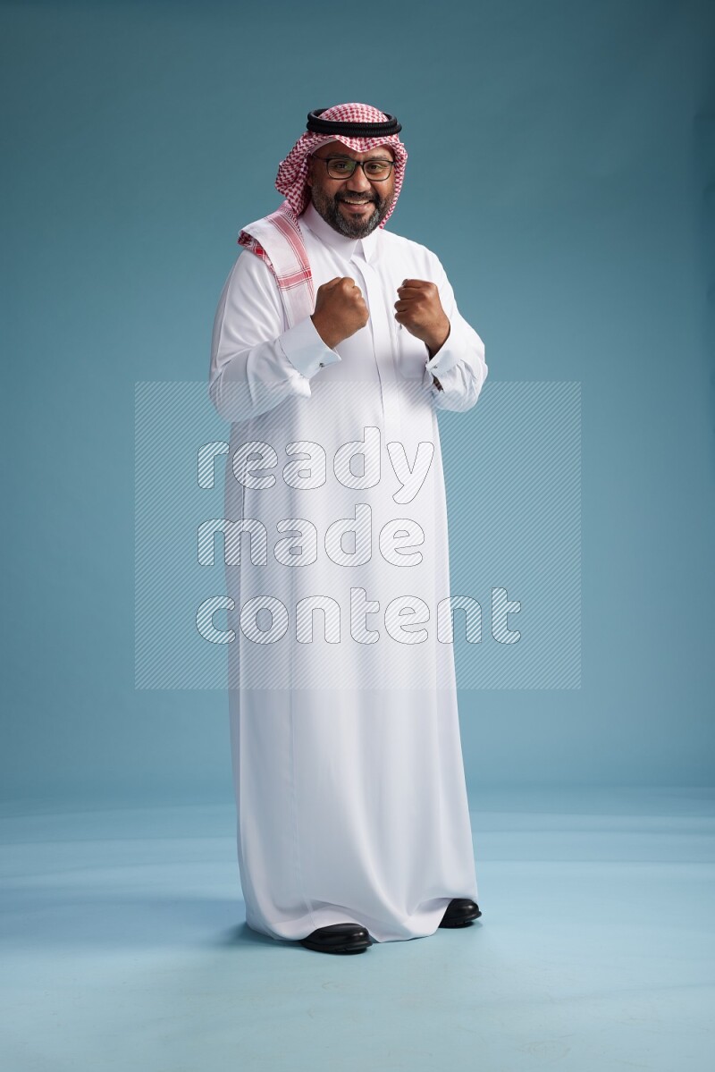 Saudi Man with shimag Standing Interacting with the camera on blue background