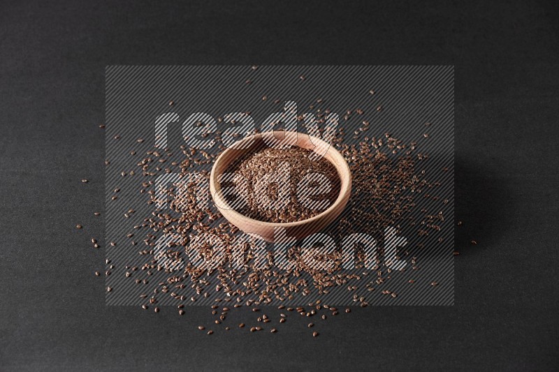 A wooden bowl full of flax surrounded by the seeds on a black flooring in different angles