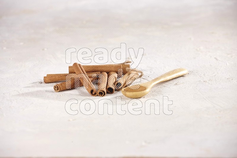 أعواد القرفة بجانب ملعقة خشبية مليئة ببودرة القرفة على خلفية بيضاء