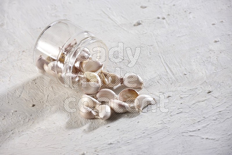 A glass jar full of garlic cloves flipped and the cloves came out on a textured white flooring in different angles
