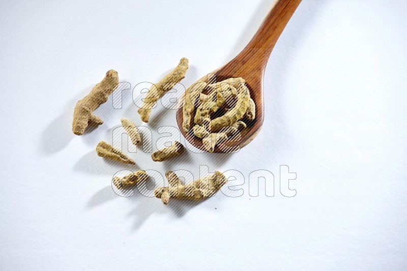 A wooden ladle full of dried turmeric fingers on white flooring