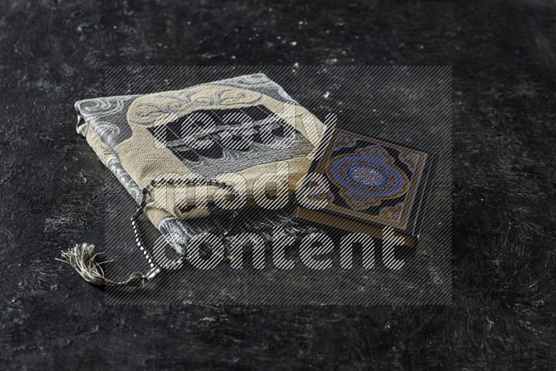 A folded prayer mat with different elements such as quran and prayer beads on black textured background