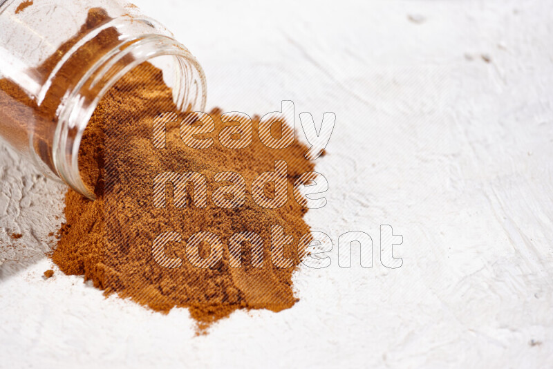 A glass jar full of ground paprika powder flipped with some spilling powder on white background