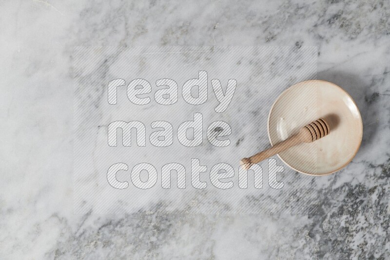 Beige pottery plate with wooden honey dipper in it on grey marble background