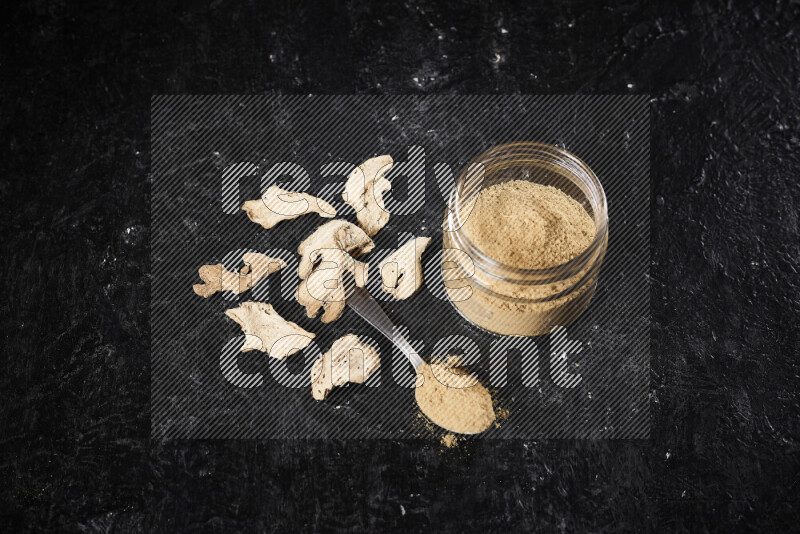 A glass jar full of ground ginger powder on black background