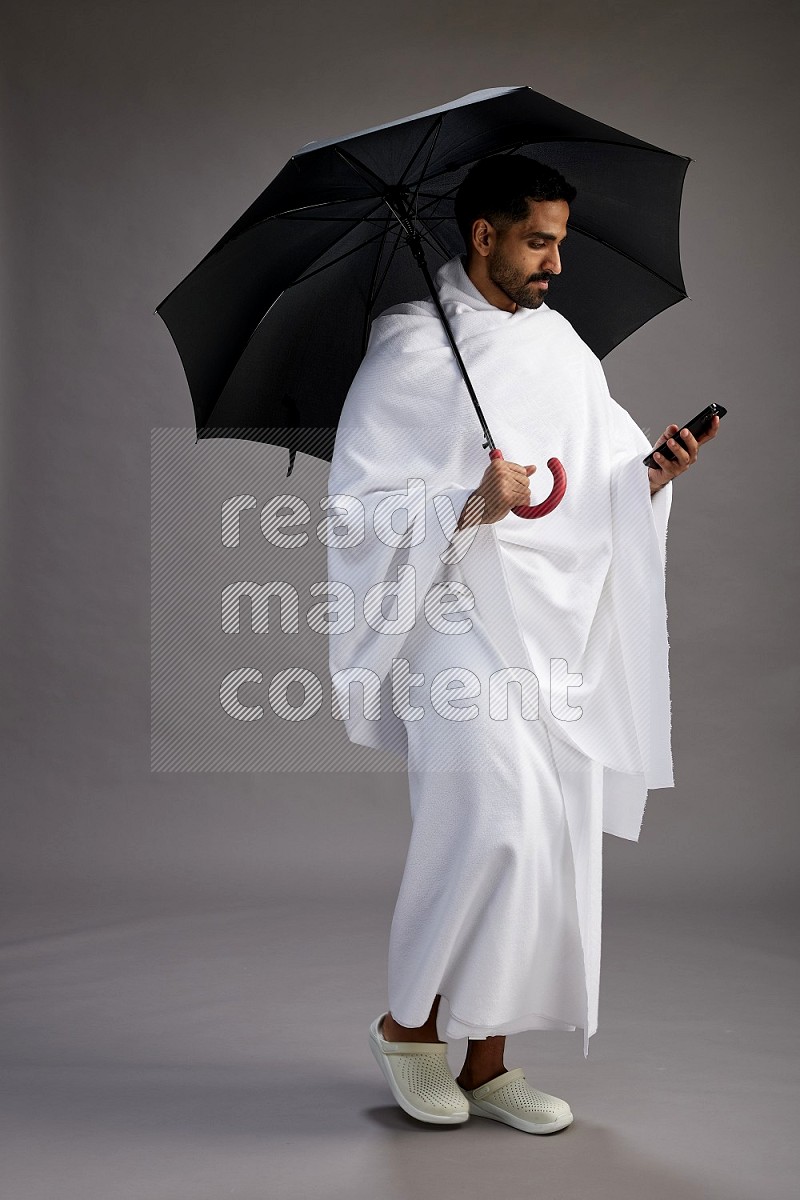 A man wearing Ehram Standing holding umbrella on gray background