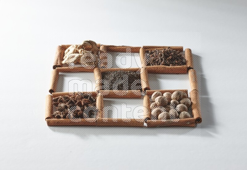 9 squares of cinnamon sticks full of tea in the middle surrounded by nutmeg, dried mint, cloves, dried basil, dried ginger, cinnamon, star anise and cardamom on white flooring