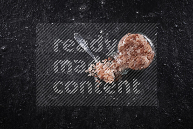 A glass jar full of coarse himalayan salt crystals on black background