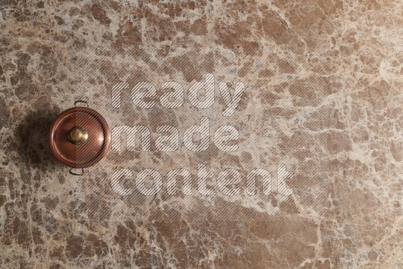 A small copper pot on beige marble background