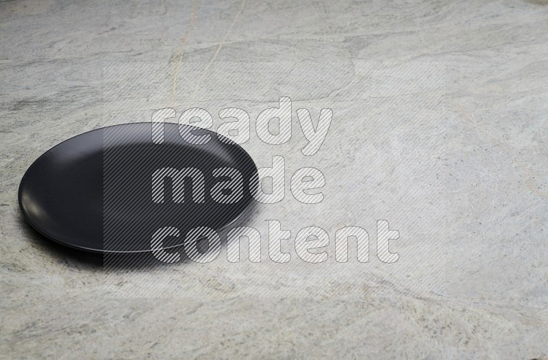 black ceramic circular plate on grey marble flooring.