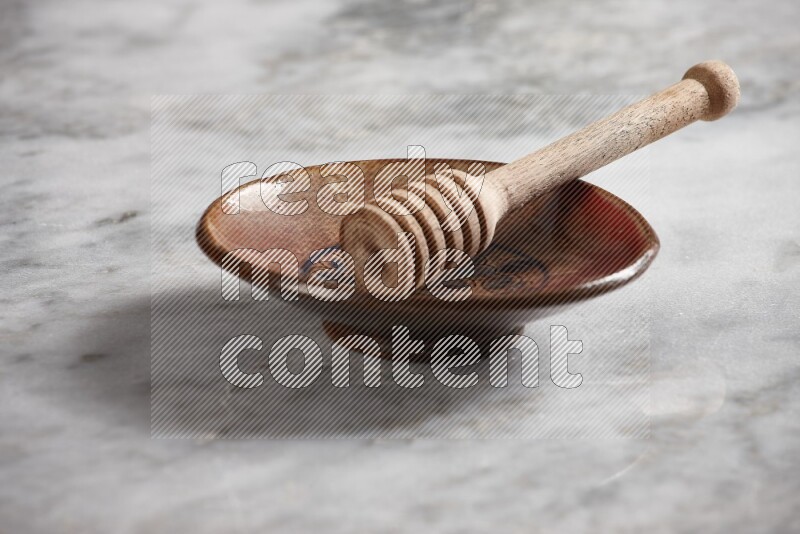 Decorative pottery plate with wooden honey dipper in it on grey marble background