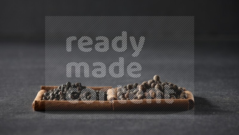 2 squares of cinnamon sticks full of black peppers and allspice on black flooring