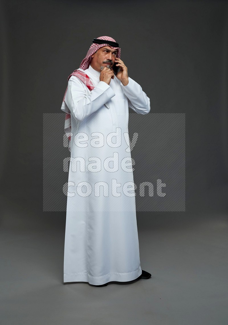 Saudi man with shomag Standing talking on phone on gray background