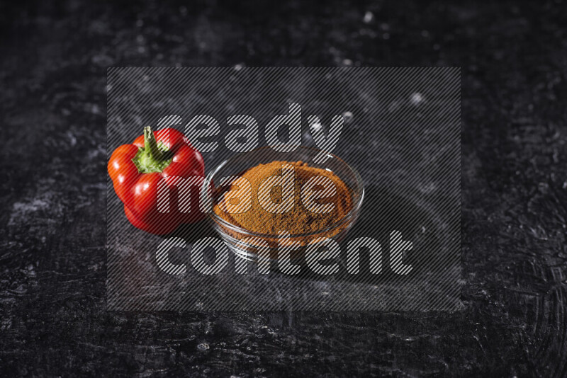 A glass bowl full of ground paprika powder on black background