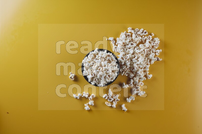 A black ceramic bowl full of popcorn with popcorn beside it on a yellow background in different angles