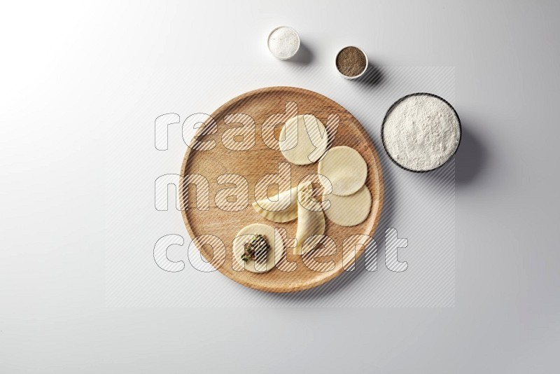 two closed sambosas and one open sambosa filled with meat while flour, salt, and black pepper aside in a wooden dish on a white background