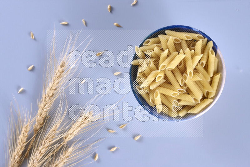 Raw pasta with wheat stalks on light blue background