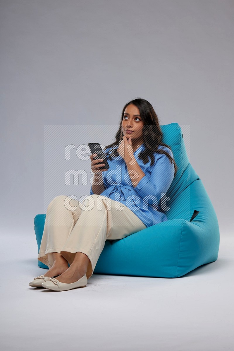 A woman sitting on a blue beanbag and texting on phone