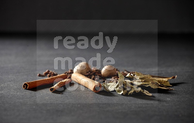 Cloves, ginger, bay laurel and cinnamon sticks on black flooring