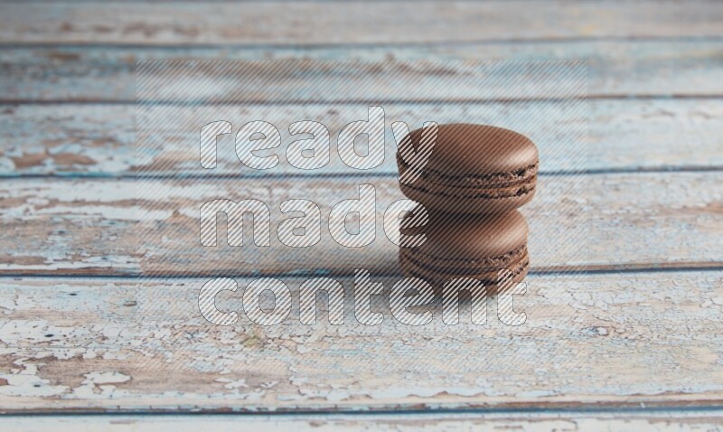 45º Shot of two Brown Dark Chocolate macarons on light blue wooden background