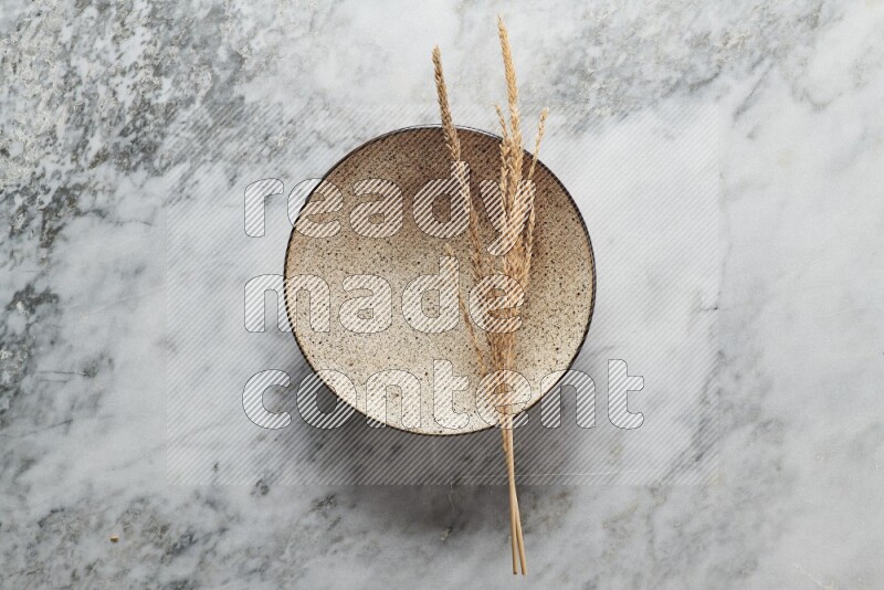 Wheat stalks on multicolored pottery plate on grey marble background