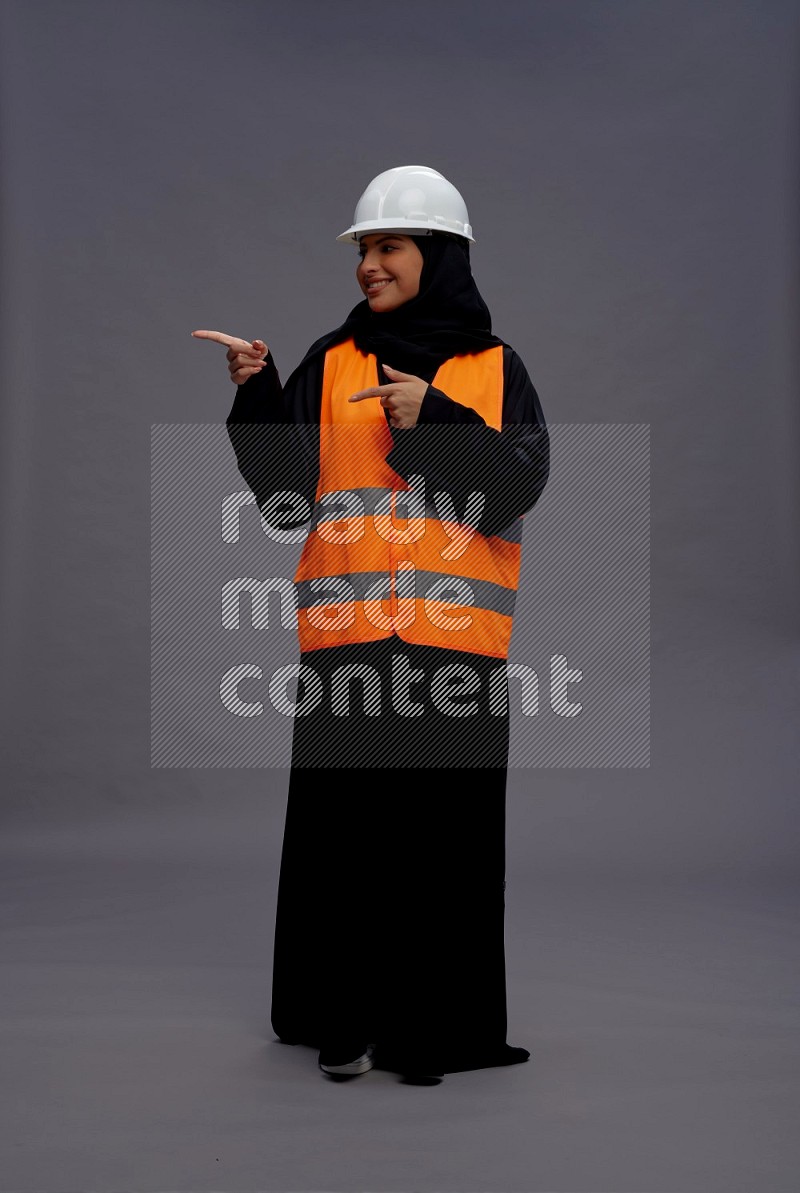 Saudi woman wearing Abaya with engineer vest standing interacting with the camera on gray background