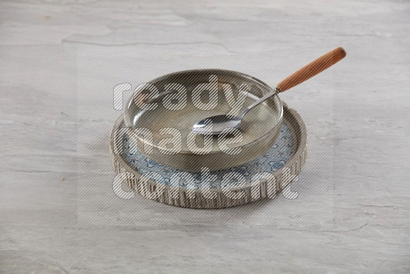 multi color pottery round dish on top of multi color round ceramic plate and spoon, on grey textured countertop