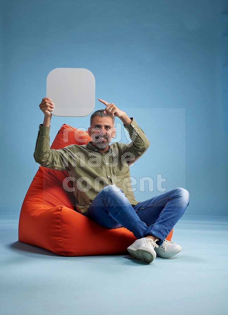 A man sitting on a orange beanbag and holding social media sign