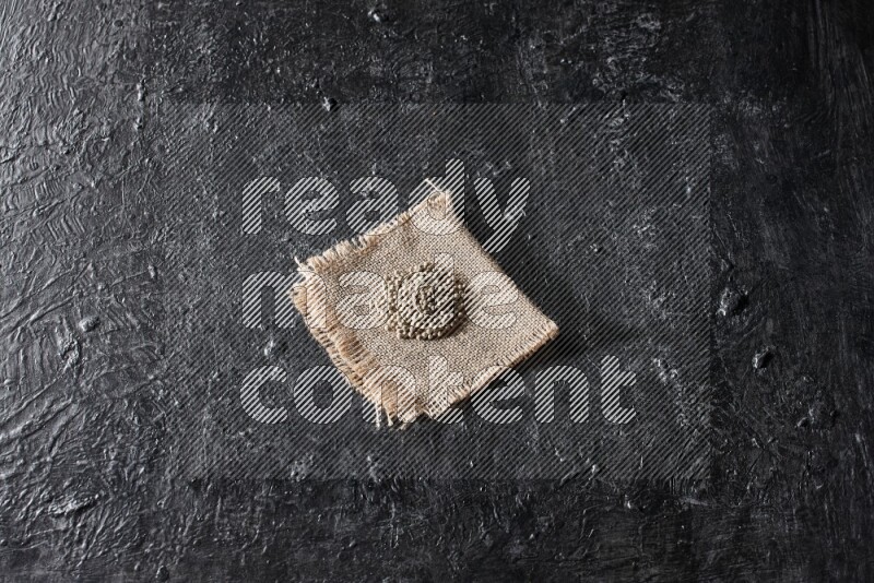 White pepper beads on a burlap piece of fabric on textured black flooring