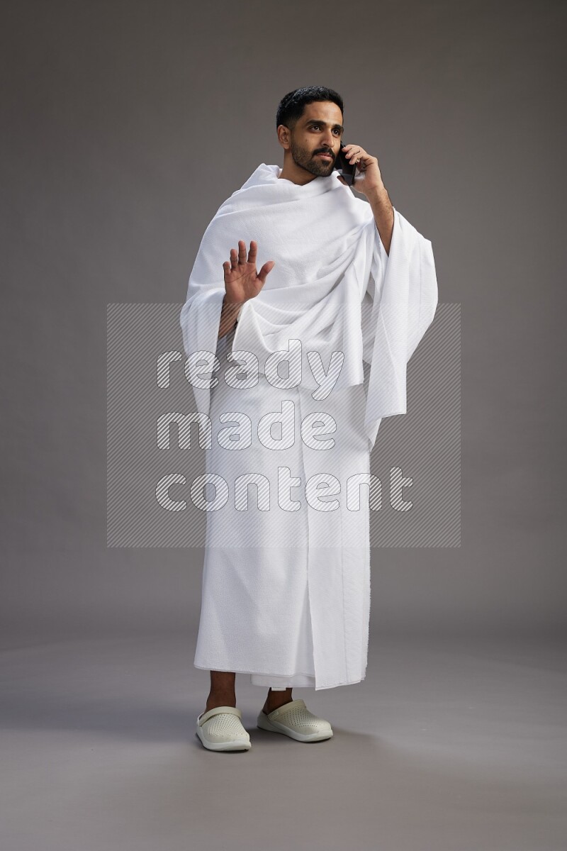 A man wearing Ehram Standing talking on phone on gray background