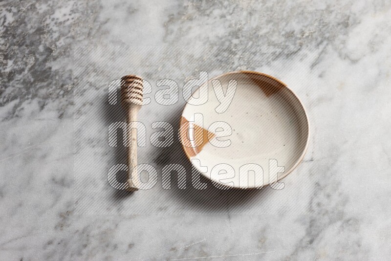 Multicolored pottery plate with wooden honey dipper on the side on grey marble background