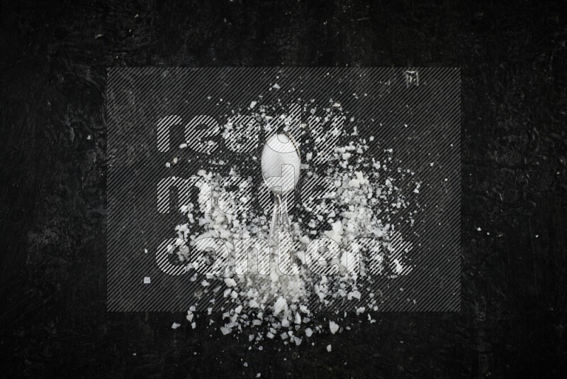 ملعقتان معدنيتان ممتلئتان بالملح الأبيض على خلفية سوداء