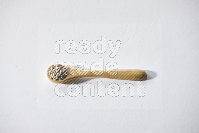 A wooden spoon full of white pepper beads on white flooring