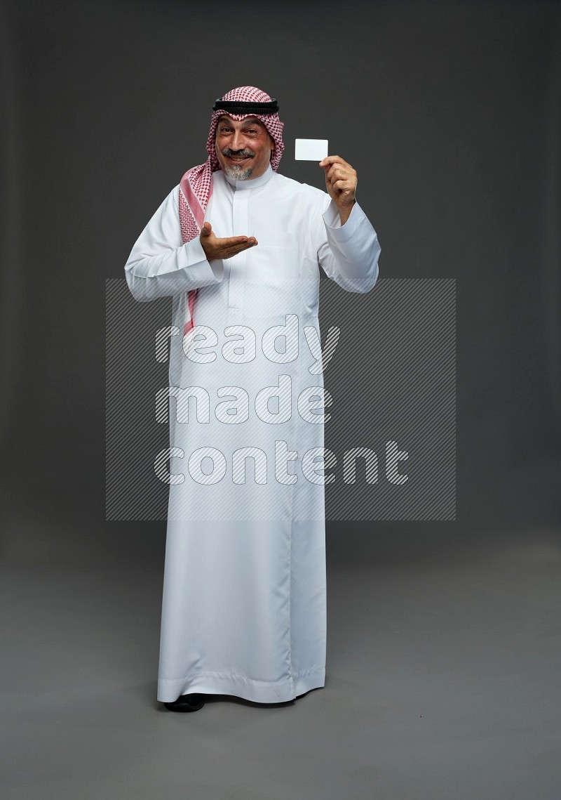 Saudi man with shomag Standing holding ATM card on gray background