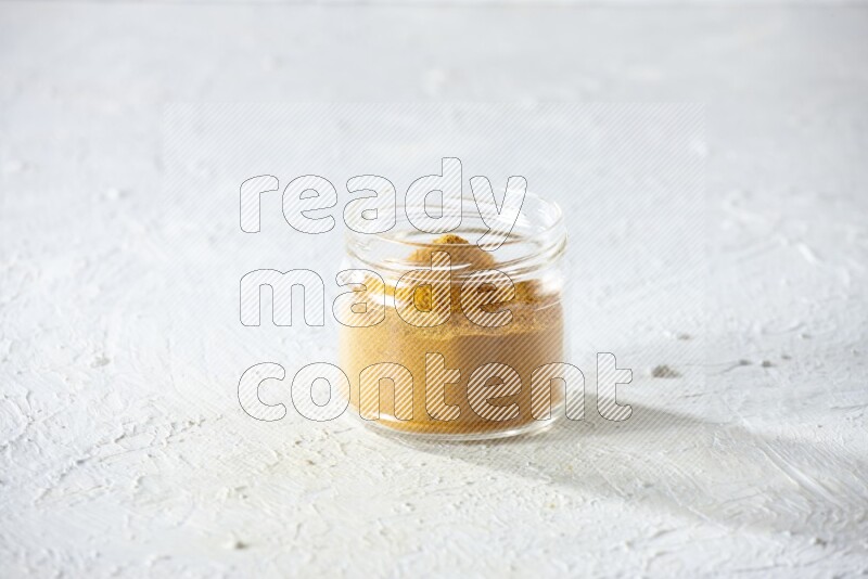A glass jar full of turmeric powder on a textured white flooring