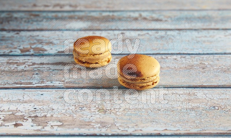 45º Shot of two Yellow Crème Brulée macarons on light blue wooden background