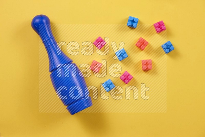 Plastic building blocks, balls and bowling pins on yellow background in top view (kids toys)