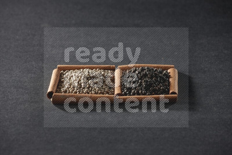 مربعان من أعواد القرفة ممتلئان بحبوب الفلفل الأبيض وحبوب الفلفل الأسود علي خلفية سوداء