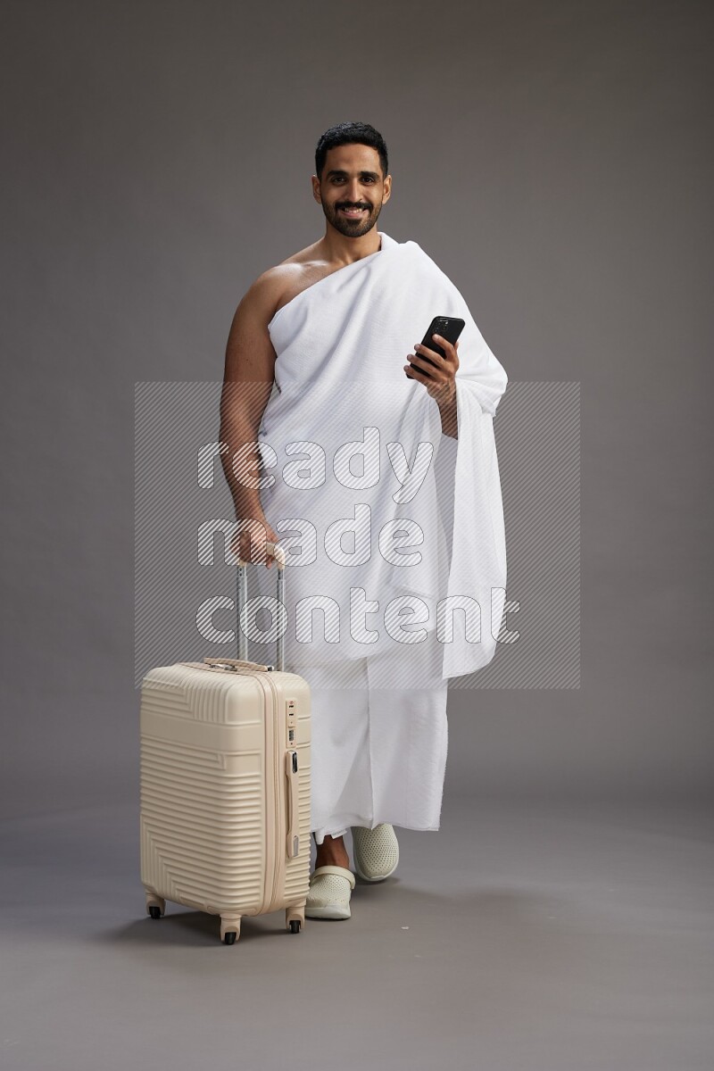 A man wearing Ehram Standing holding traveling bag on gray background
