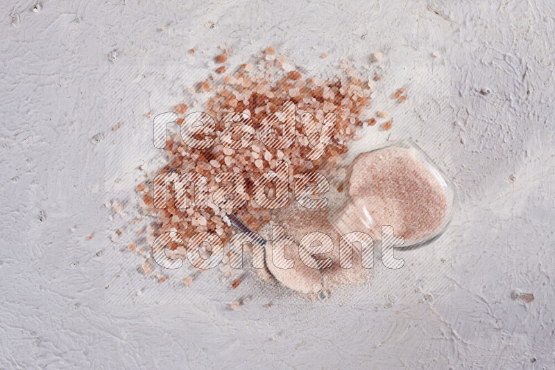 A glass jar full of fine himalayan salt with some himalayan crystals beside it on a white background