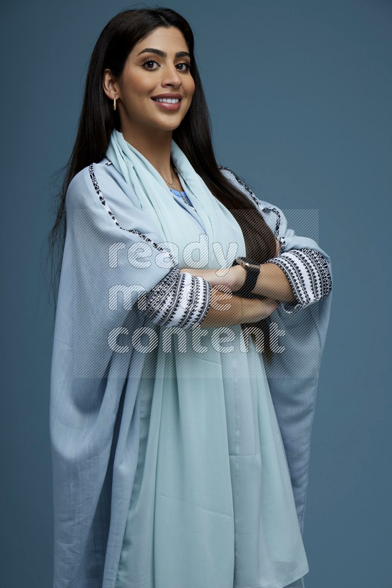 A woman posing in a blue background wearing blue Abaya no Hijab