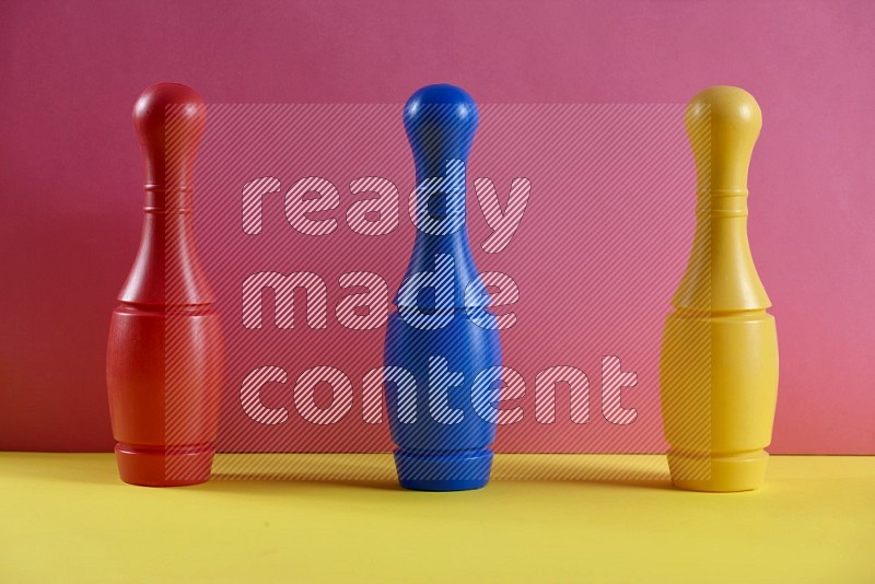 Plastic bowling pins with balls on pink and yellow background (kids toys)