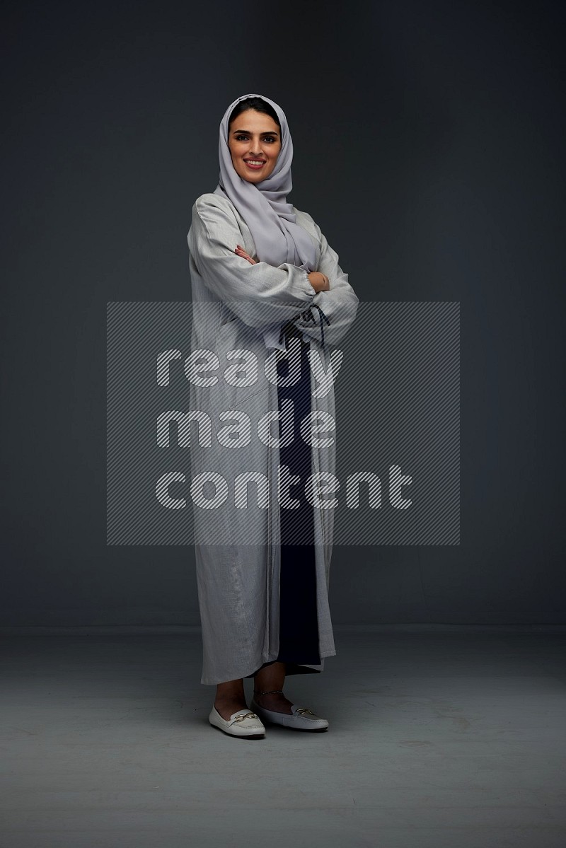 A Saudi woman wearing a light gray Abaya and head scarf standing and making multi poses eye level on a grey background