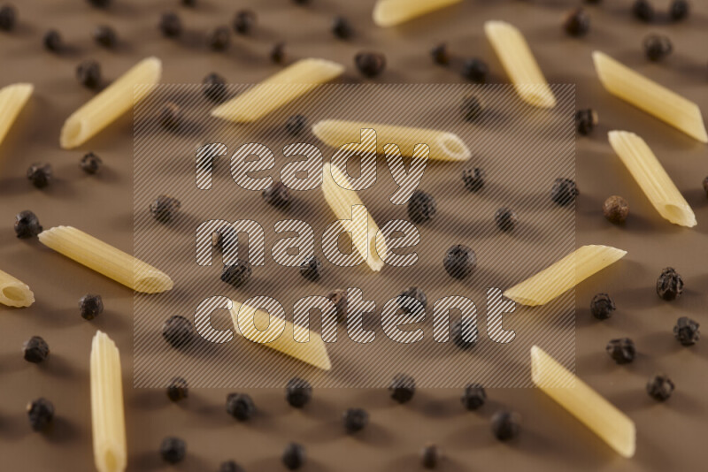 Raw pasta with different ingredients such as cherry tomatoes, garlic, onions, red chilis, black pepper, white pepper, bay laurel leaves, rosemary and cardamom on beige background